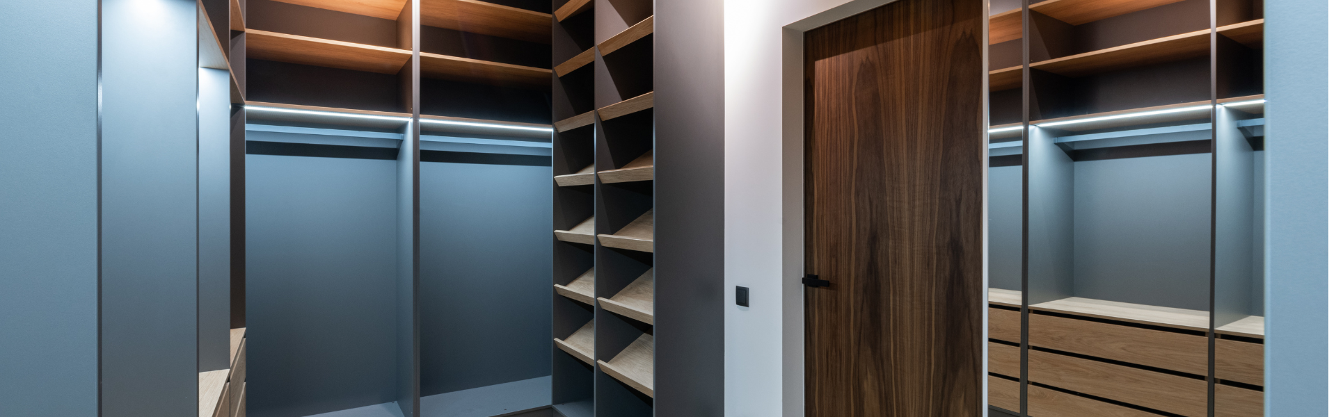 Moderner begehbarer Kleiderschrank mit grauen Regalen, Holzschubladen und heller Holzoptik am Boden.