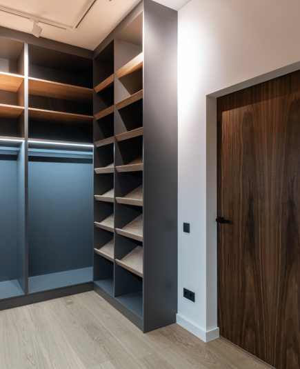 Moderner begehbarer Kleiderschrank mit grauen Regalen, Holzschubladen und heller Holzoptik am Boden.