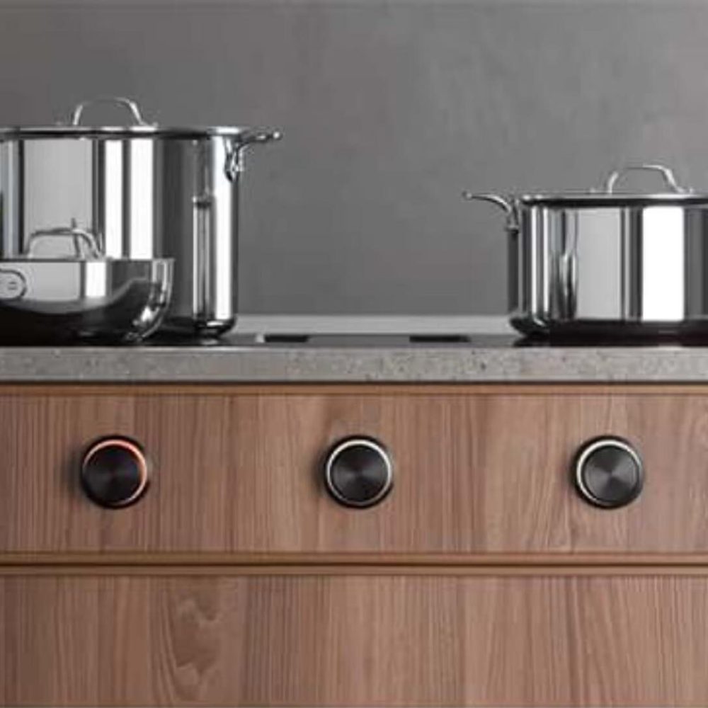 Moderne Küche mit glänzenden Edelstahltöpfen auf einem eleganten Kochfeld mit schwarzen Drehknöpfen.