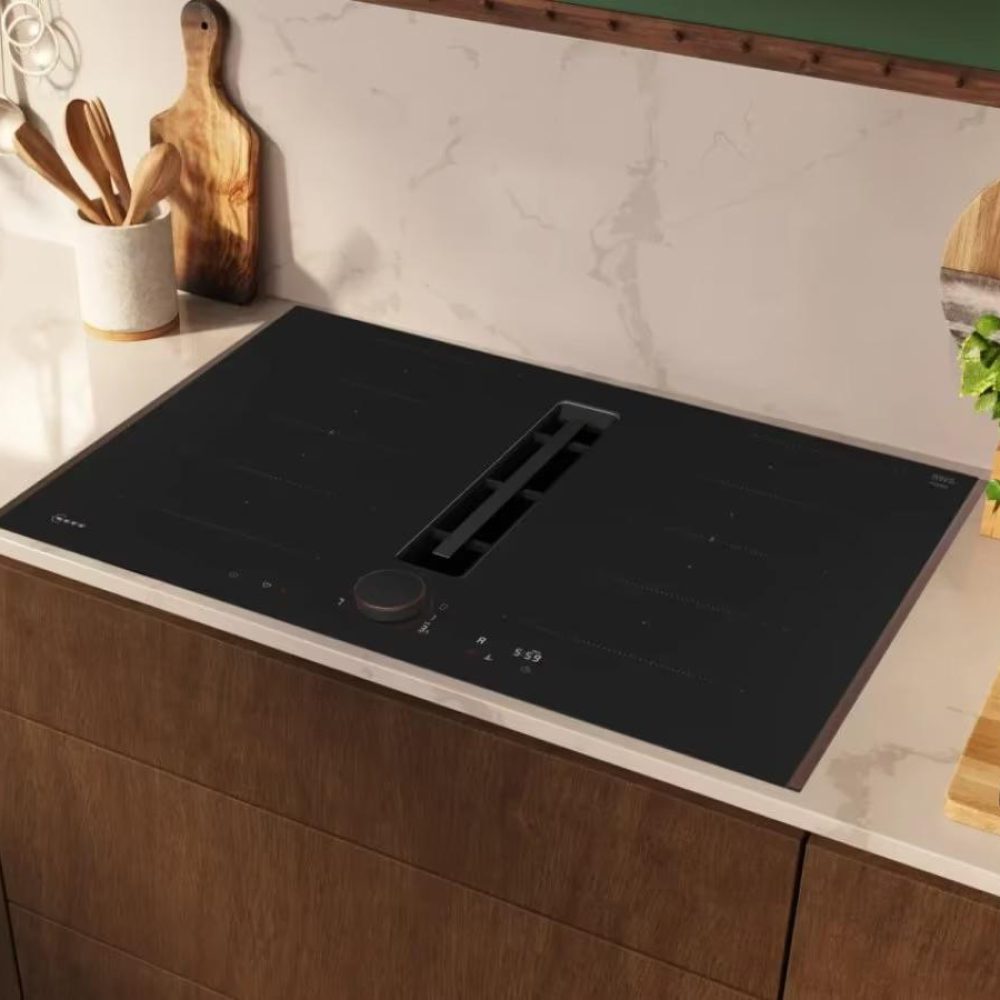 Moderne Küche mit Induktionskochfeld, kupfernem Wasserhahn und Schneidebrett mit Obst und Nüssen.